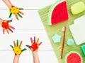 Manos pintadas de colores con caritas sonrientes, listas para hacer jabones para niños. Hay jabones con forma de sandía y otros accesorios de baño.