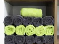Estantería con toallas enrolladas en gris y verde lima. Una toalla pequeña personalizada, doblada encima, lista para usar.