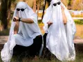 Dos figuras cubiertas con sábanas blancas y gafas de sol, sentadas en un banco de piedra. Una mira su reloj, la otra extiende la mano. ¡Ideas de terror para un disfraz!