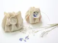 Dos pequeños paquetes de tela rústica, atados con hilo y sellados con cera, decorados con flores secas. Son detalles de boda originales hechos a mano, perfectos para un toque natural.