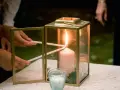 Manos encienden velas finas de una vela principal dentro de un farol dorado. Una escena de la ceremonia de las velas.