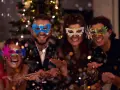 Cuatro amigos disfrutan de una temática fiesta de mascaras, riendo y lanzando confeti frente a un árbol de Navidad iluminado.