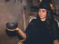 Mujer con disfraz bruja casero adulto, con sombrero negro y naranja, sosteniendo un cuenco humeante.