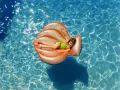 Niña sonriente en un flotador naranja con forma de concha, disfrutando de la pool party y sus juegos bajo el sol.