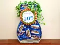 Un jarrón lleno de botes de chuches caseros, decorado con un lazo verde y un mensaje que dice "BIRTHDAYS are a JOY".