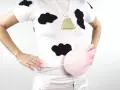 Persona con un disfraz vaca casero: camiseta blanca con manchas negras, collar de campana dorada y un globo rosa simulando la ubre.