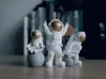 Tres figuras de un disfraz astronauta casero, una meditando sobre la luna, otra celebrando y la tercera jugando con una pequeña luna.