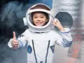 Niña sonriente con un disfraz de universo casero de astronauta, pulgar arriba, lista para explorar.