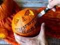 Creando una calabaza de Halloween fácil. Un cuchillo talla una sonrisa dentada en una calabaza naranja, con ojos triangulares ya cortados.