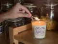 Encendiendo una vela decorada, parte de manualidades para decorar velas, con frascos de vidrio de fondo.