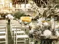 Sillas blancas alineadas en un jardín, un sofá amarillo y un gran arreglo floral. Ideas para como hacer una boda económica y hermosa.