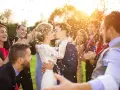 Novios besándose entre confeti mientras amigos aplauden y ríen. ¡Un momento perfecto para felicitar a unos novios!