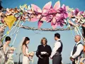 Boda al aire libre con un arco decorado con manualidades de papel coloridas. La pareja se da el sí ante un oficiante.