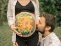Barriga de embarazada pintada con un león y el nombre "Leo". El padre besa la barriga. Unas plantillas para pintar barriga de embarazada niño, como esta, son un recuerdo precioso.