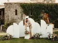 Pareja besándose frente a un photocall bodas de oro casero, decorado con flores y un fondo arquitectónico.
