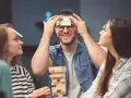 Amigos jugando a "adivina la palabra" en su frente, parte de juegos para fiestas adultos.