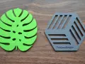 Posavasos de fieltro verde con forma de hoja y otro gris hexagonal con líneas, sobre fondo de madera.
