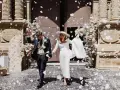 Novios felices salen de la iglesia, cubiertos de pétalos blancos. Es un momento perfecto para tirar confeti en una boda.