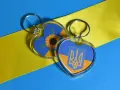 Dos llaveros en forma de corazón con la bandera de Ucrania. Uno tiene un girasol, el otro el escudo. Ideas para como hacer llaveros personalizados.