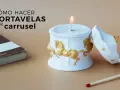 Portavelas manualidades de carrusel, blanco con caballos dorados, junto a un libro y una cerilla.