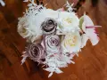 Un ramo de novia con rosas blancas y lilas, helechos blancos y una flor de anthurium rosa. Un recuerdo para secar y atesorar.
