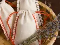 Bolsitas perfumadas para armarios caseras, hechas a mano con tela de lino y cordones rojos, junto a un manojo de lavanda seca en una cesta de mimbre.