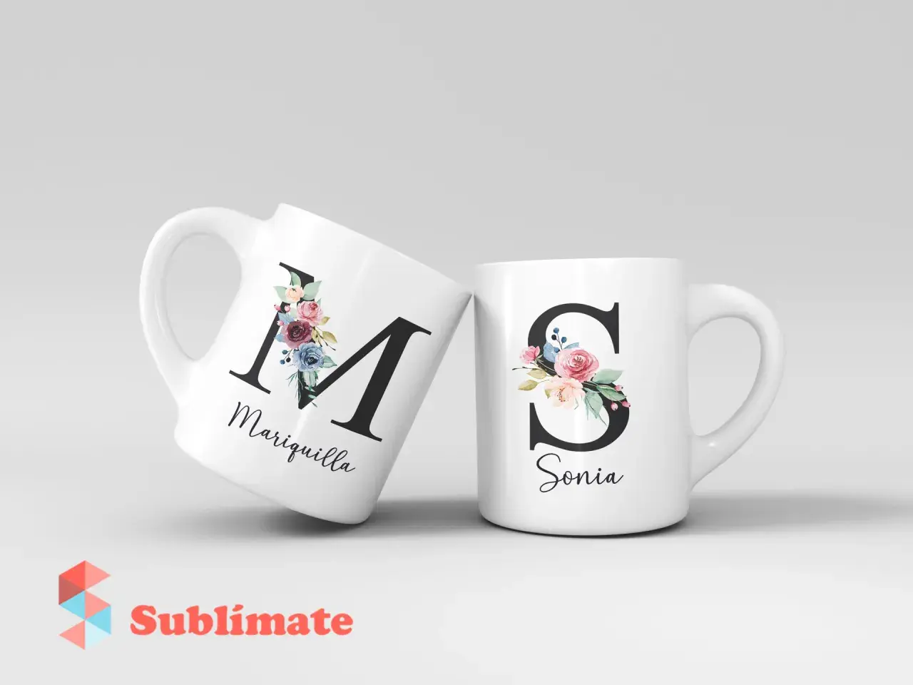 Dos tazas blancas con iniciales decoradas con flores. Una tiene la "M" de Mariquilla, la otra la "S" de Sonia.