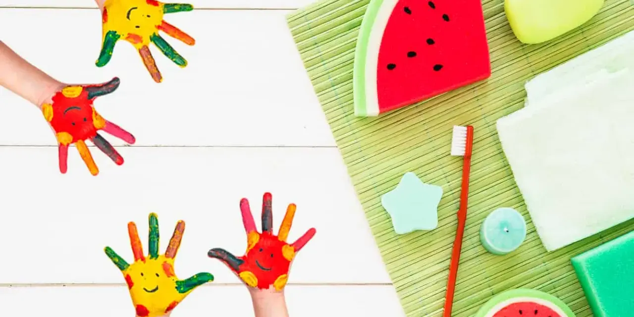 Manos pintadas de colores con caritas sonrientes, listas para hacer jabones para niños. Hay jabones con forma de sandía y otros accesorios de baño.