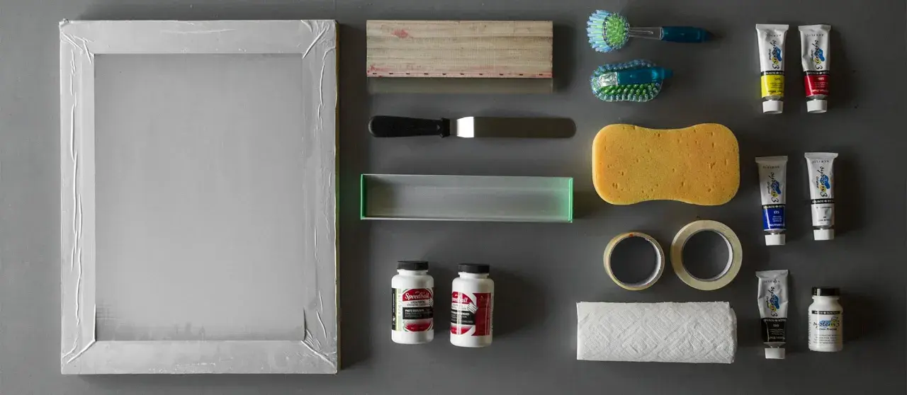 Marco de serigrafía, rasquetas, esponja, cintas, papel, cepillos y tubos de pintura acrílica, todo listo para empezar con los materiales serigrafia.