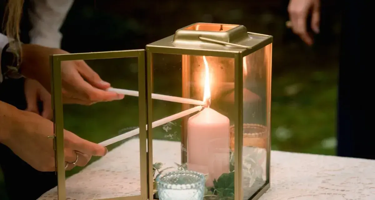 Manos encienden velas finas de una vela principal dentro de un farol dorado. Una escena de la ceremonia de las velas.