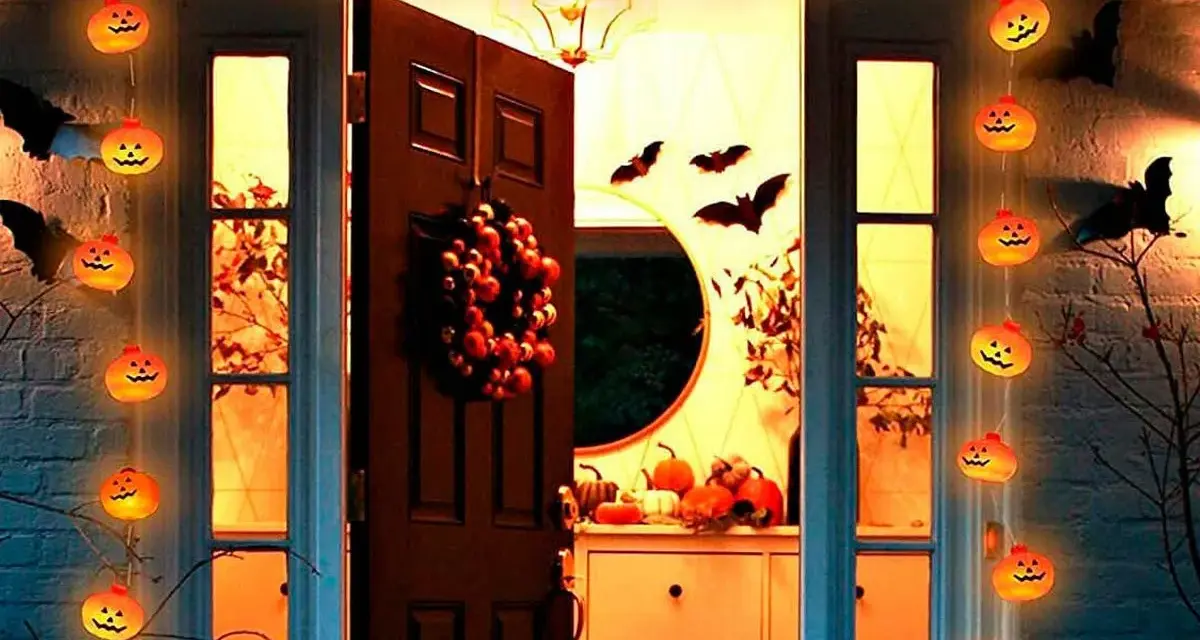 Guirnalda de calabazas iluminadas y murciélagos de cartón crean una espeluznante decoración de terror casera frente a una puerta.