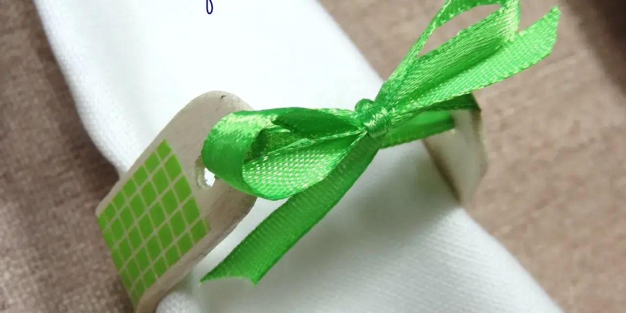 Servilleteros caseros originales: un detalle de madera con cinta verde brillante y patrón de cuadros, atado a una servilleta blanca.