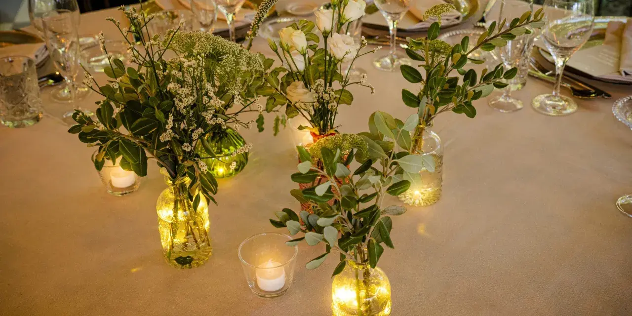 Elegante decoracion con velas y flores en jarrones de cristal, creando un ambiente cálido y acogedor para una cena especial.