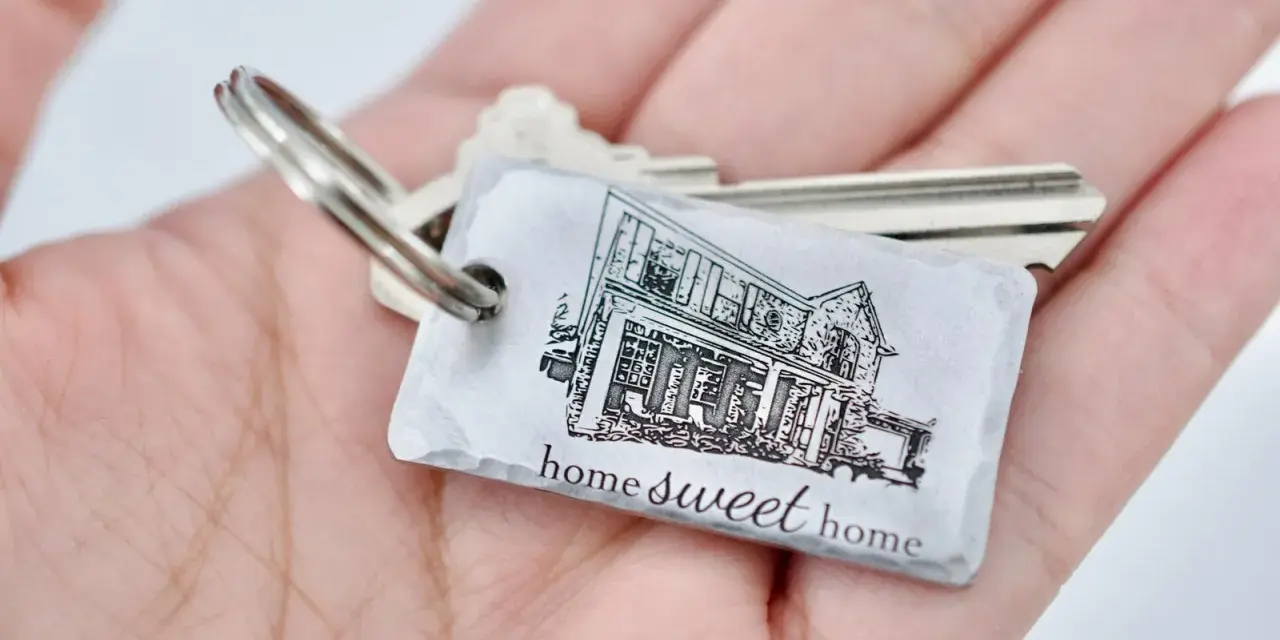 Un llavero hogar con la imagen de una casa y la frase "home sweet home" descansa en una mano.