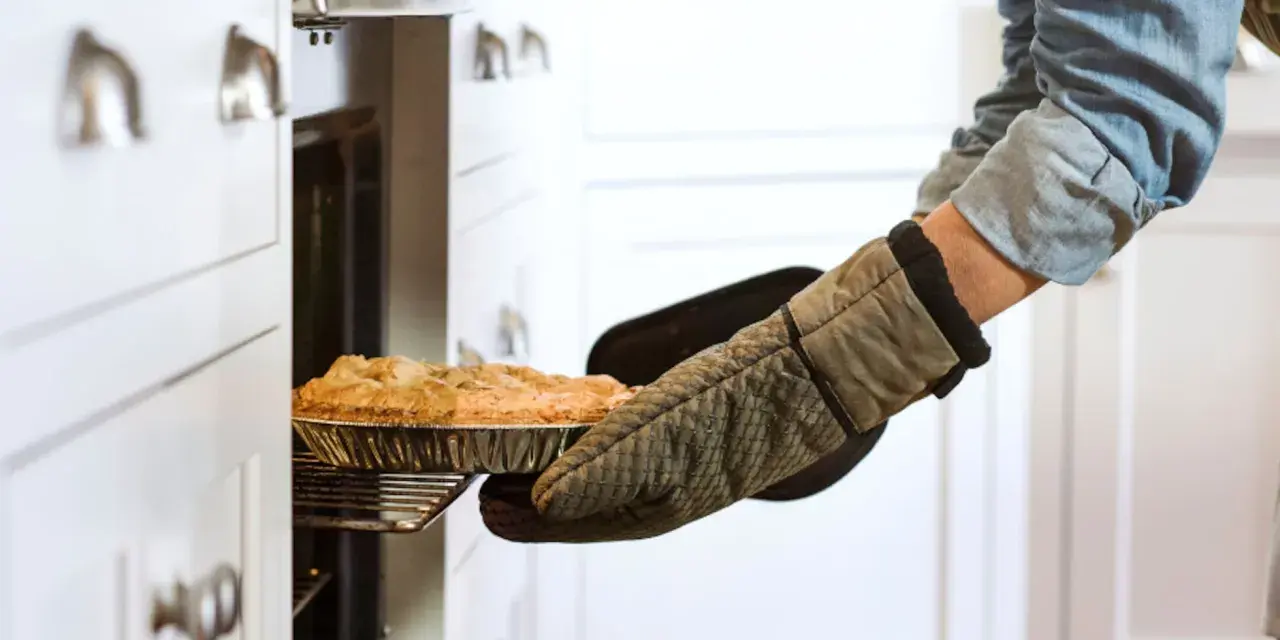 Persona saca un pastel del horno con guantes de cocina personalizados.