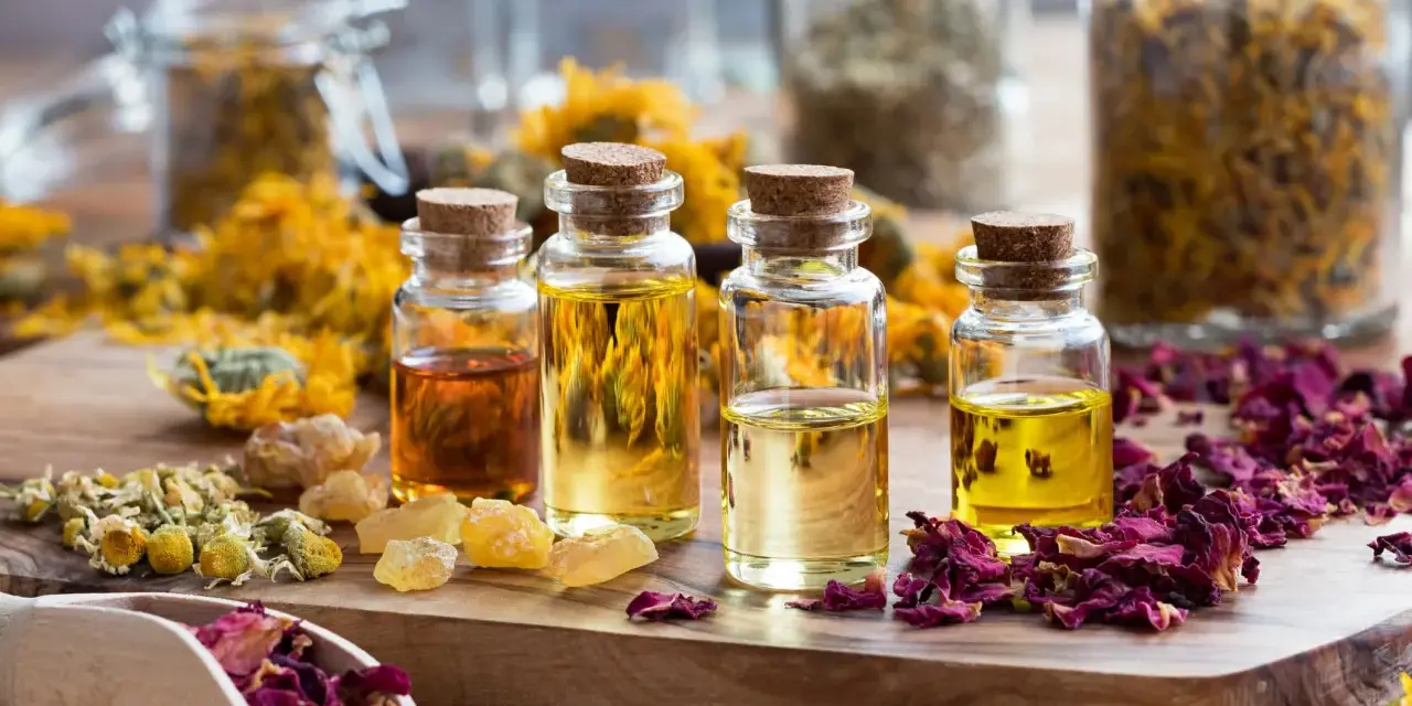 Botellas con aceites esenciales y pétalos de rosa, manzanilla y caléndula. Ideas para saber como hacer esencias aromaticas caseras.