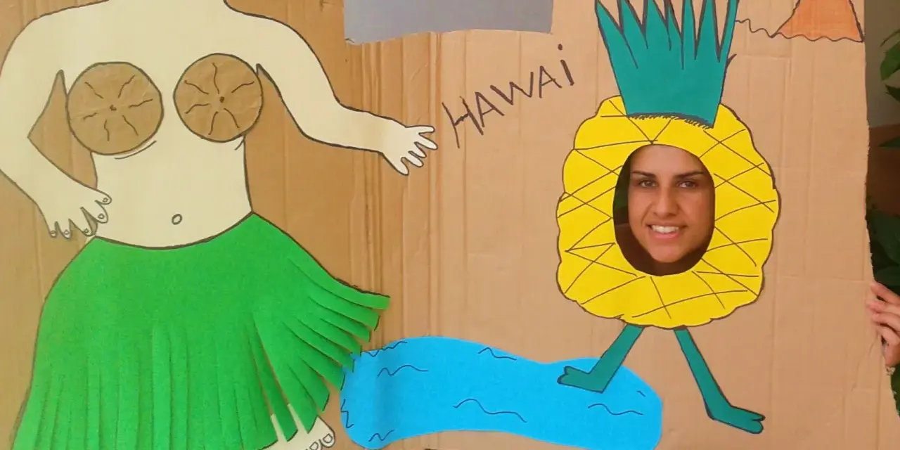 Divertido photocall hawaiano casero con una figura de bailarina y una piña con cara sonriente. ¡Perfecto para unas fotos tropicales!