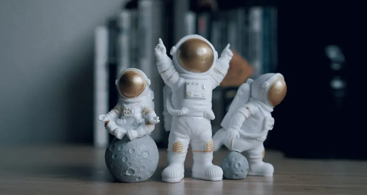 Tres figuras de un disfraz astronauta casero, una meditando sobre la luna, otra celebrando y la tercera jugando con una pequeña luna.
