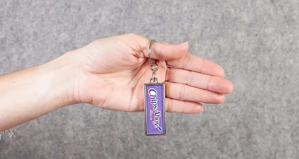 Mano sosteniendo un llavero personalizado con el logo de "Chips Ahoy!". Ideal para quienes buscan dónde hacer llaveros personalizados.