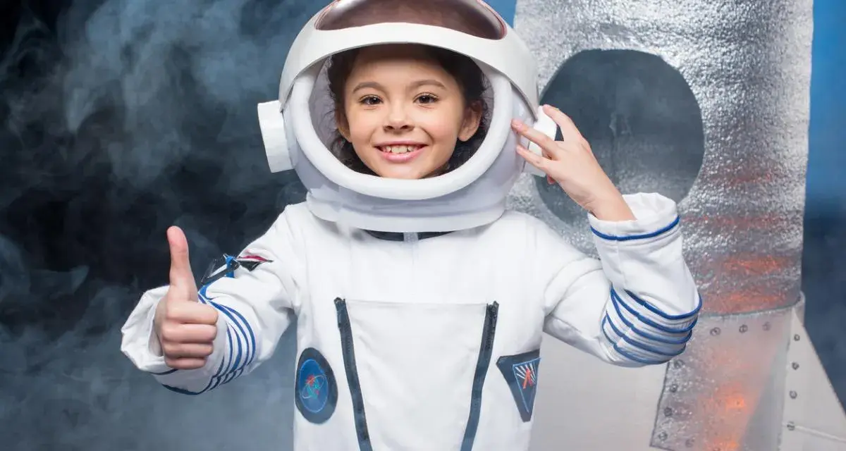 Niña sonriente con un disfraz de universo casero de astronauta, pulgar arriba, lista para explorar.