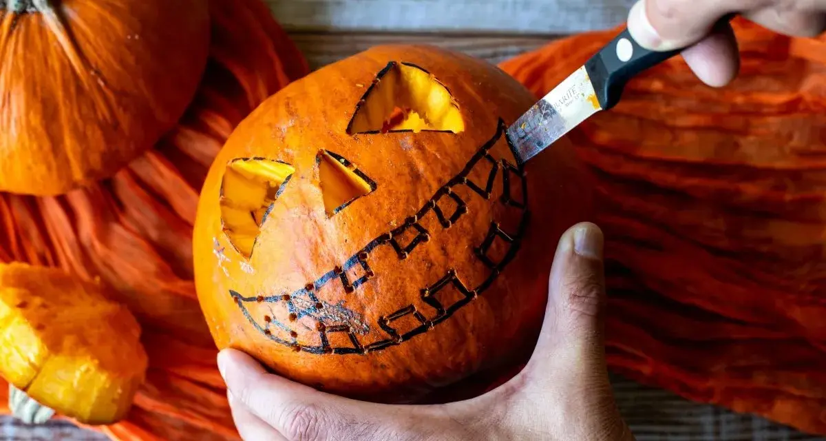 Creando una calabaza de Halloween fácil. Un cuchillo talla una sonrisa dentada en una calabaza naranja, con ojos triangulares ya cortados.
