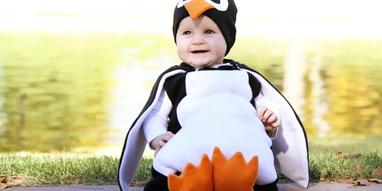 Bebé sonriente con un adorable disfraz pinguino casero, con aletas y pico naranja.