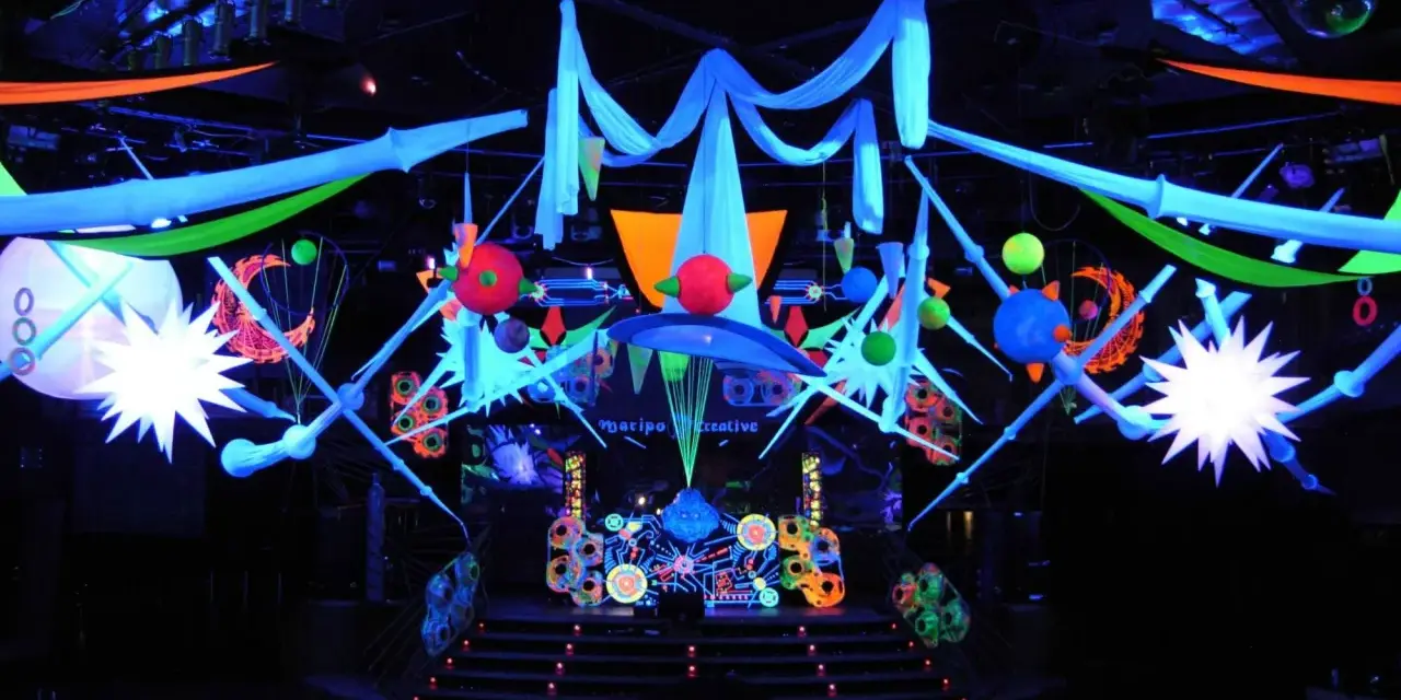 Decoración vibrante para una fiesta futurista, con luces neón, telas colgantes y estructuras geométricas que crean un ambiente de otro mundo.