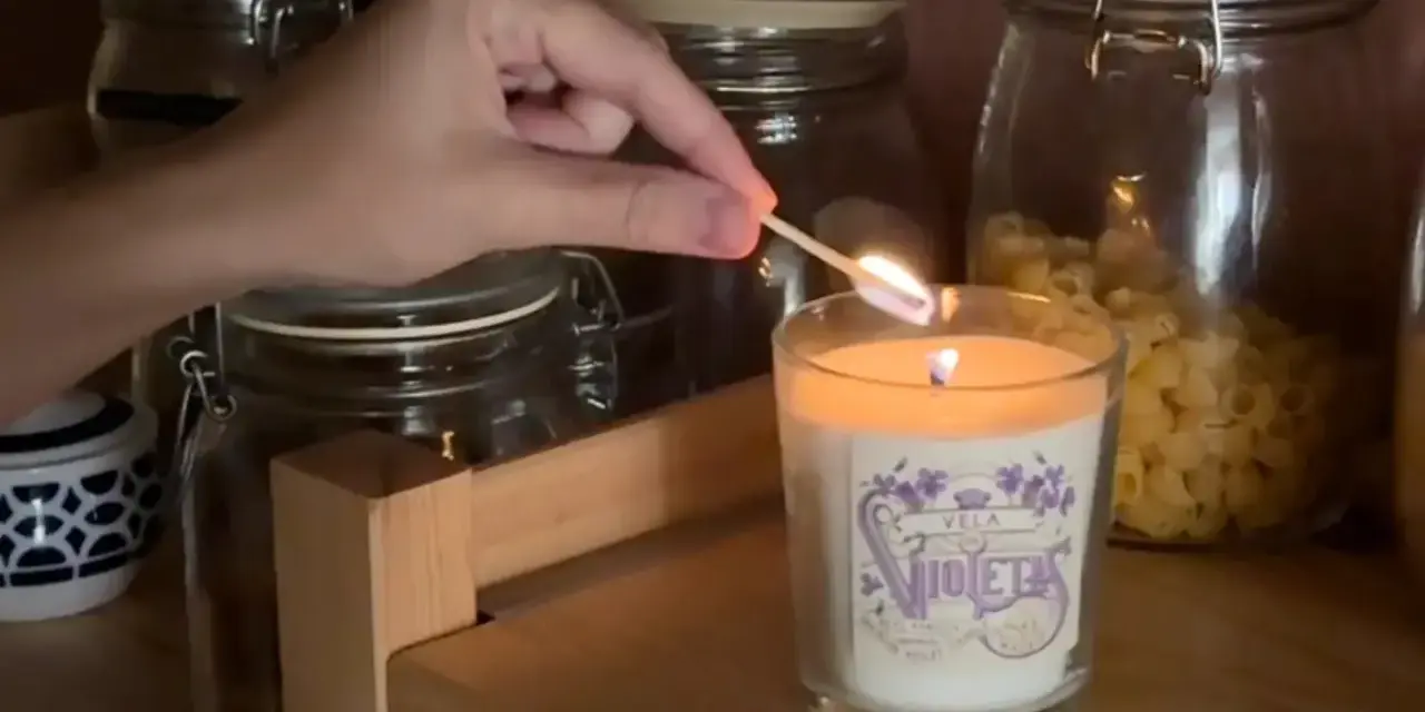 Encendiendo una vela decorada, parte de manualidades para decorar velas, con frascos de vidrio de fondo.