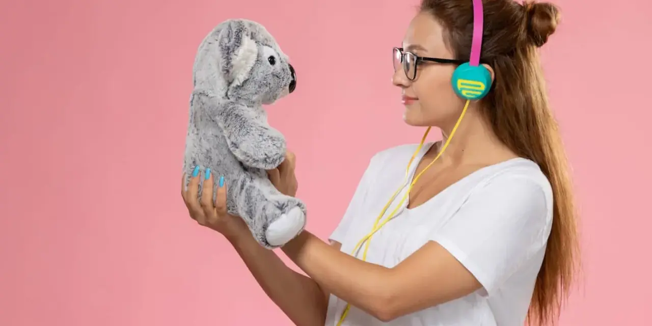 Mujer con auriculares sostiene un peluche de koala gris, como si compartieran secretos. ¡Un par de osos personalizados para la diversión!