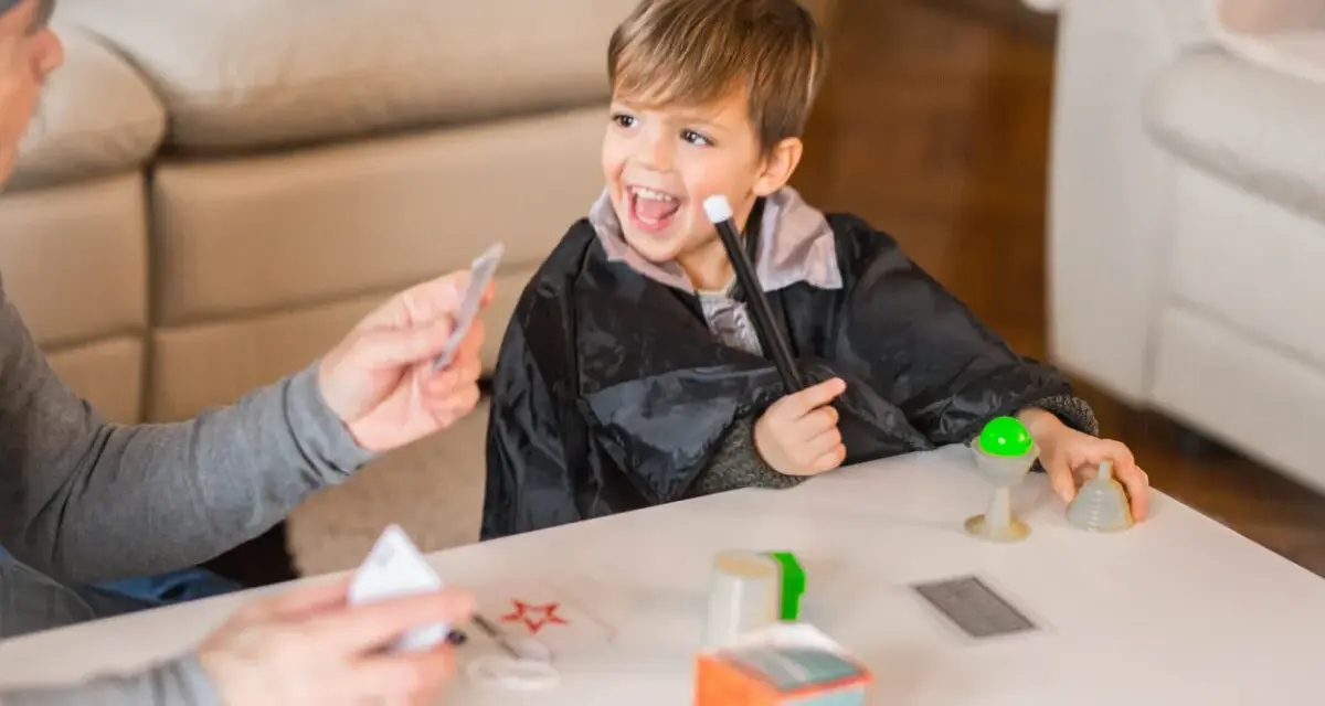 Niño con túnica de mago practica trucos de magia para niños con las manos, usando varita y cartas.