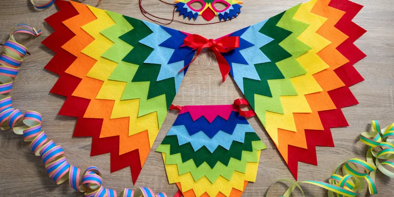 Un colorido disfraz de pájaro casero con alas de fieltro, máscara y adornos de serpentinas, listo para una fiesta.