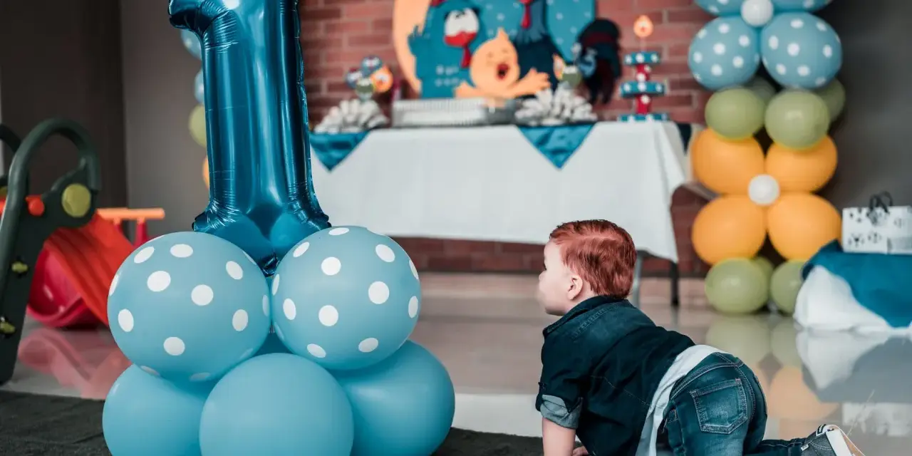 Niño gateando junto a globos azules y un gran número 1. Ideas para como preparar una fiesta infantil barata y muy original.