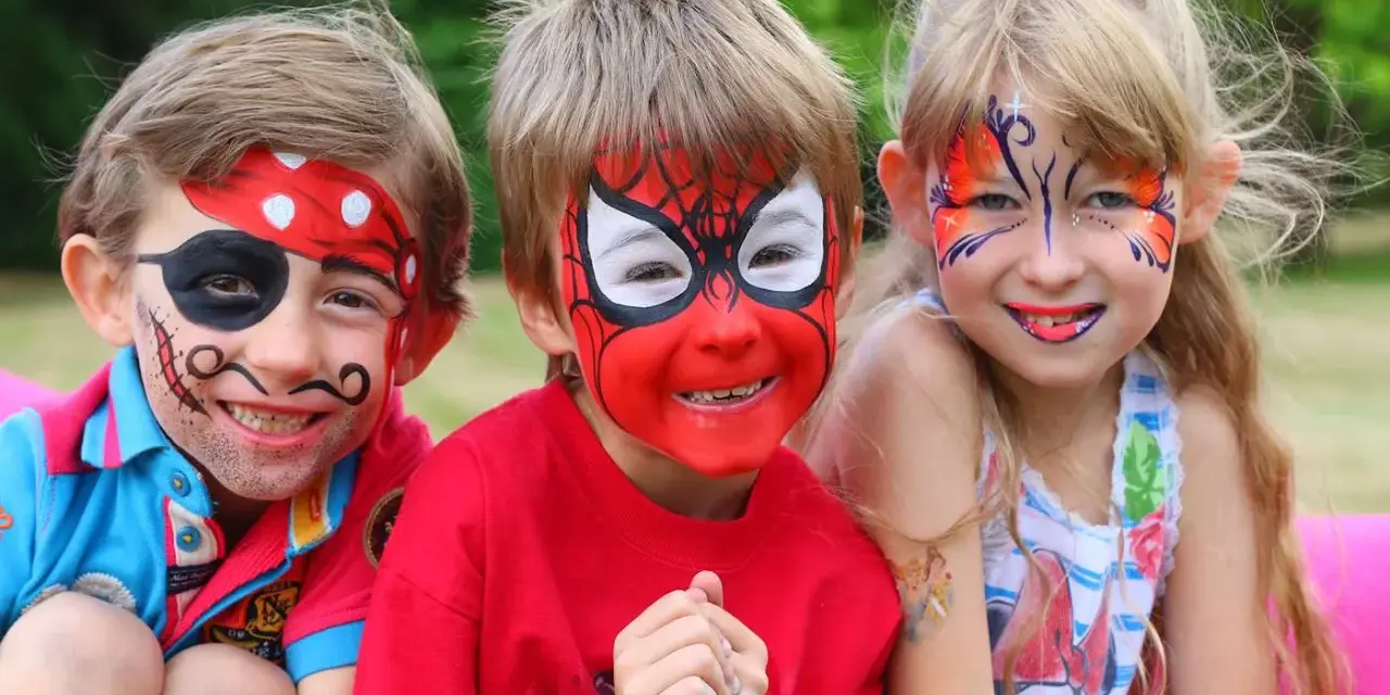 Niños con pintacaras de pirata, Spider-Man y mariposa sonriendo.