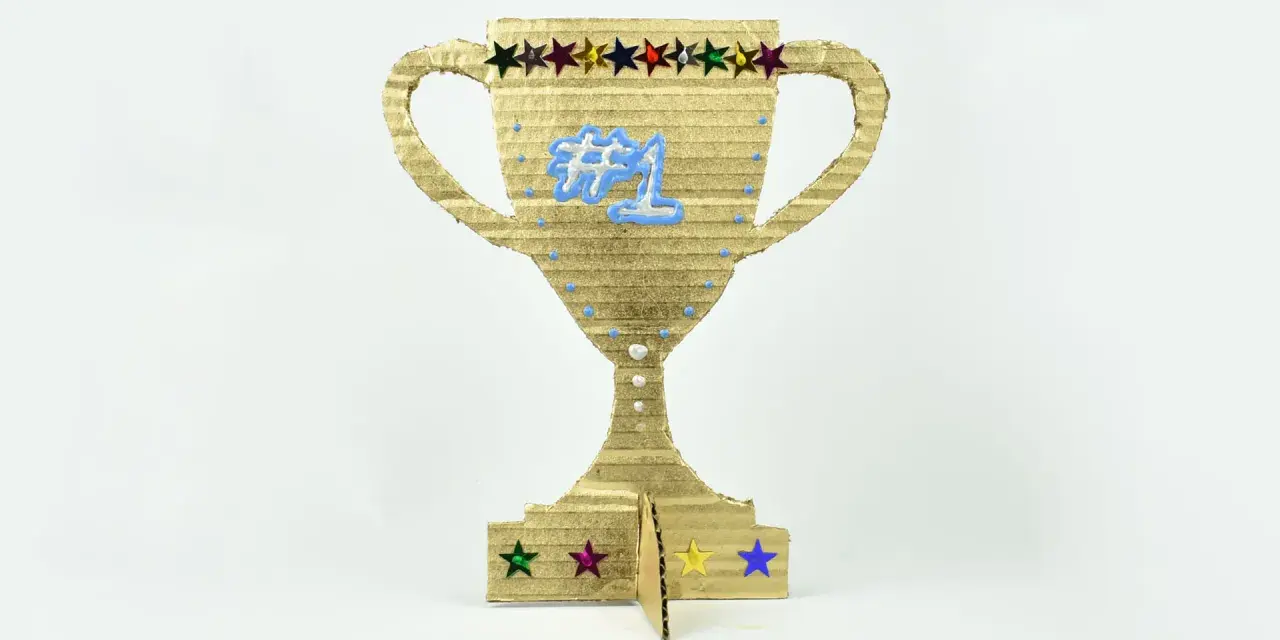 Trofeo de cartón dorado, ideal para hacer trofeos personalizados. Luce un "#1" azul y estrellas de colores.